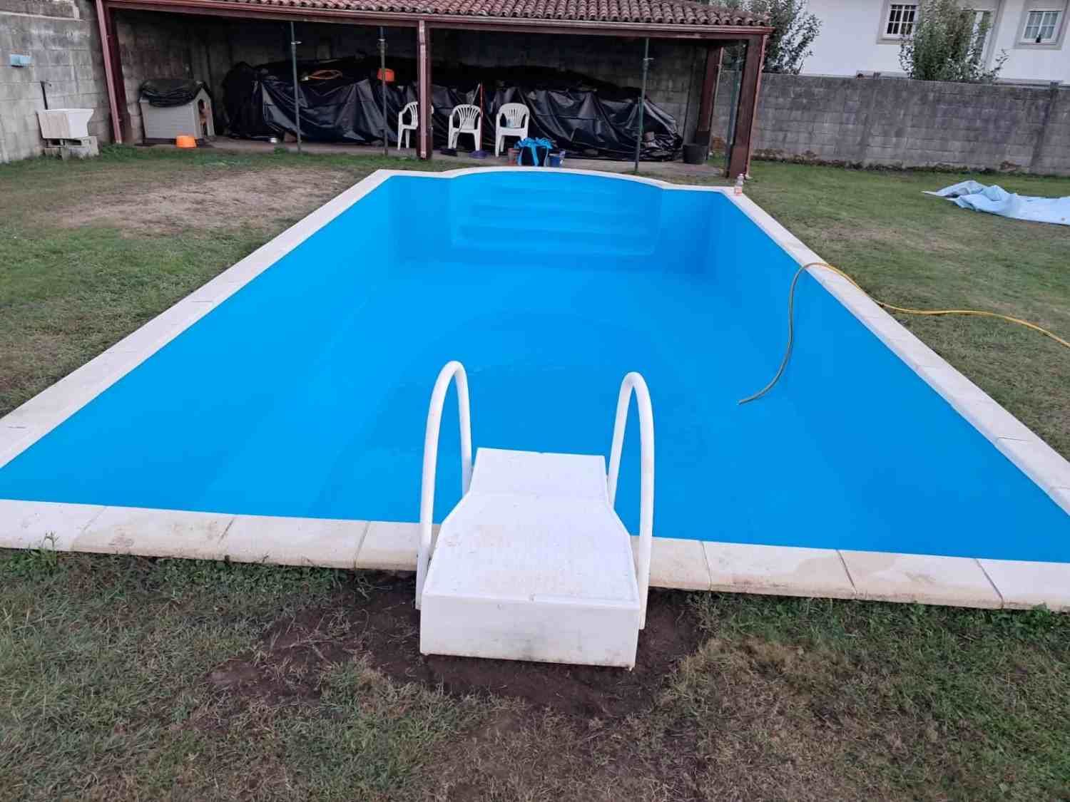 Piscina vacía azul en el patio trasero, con una escalera blanca y un trampolín frente a un patio cubierto