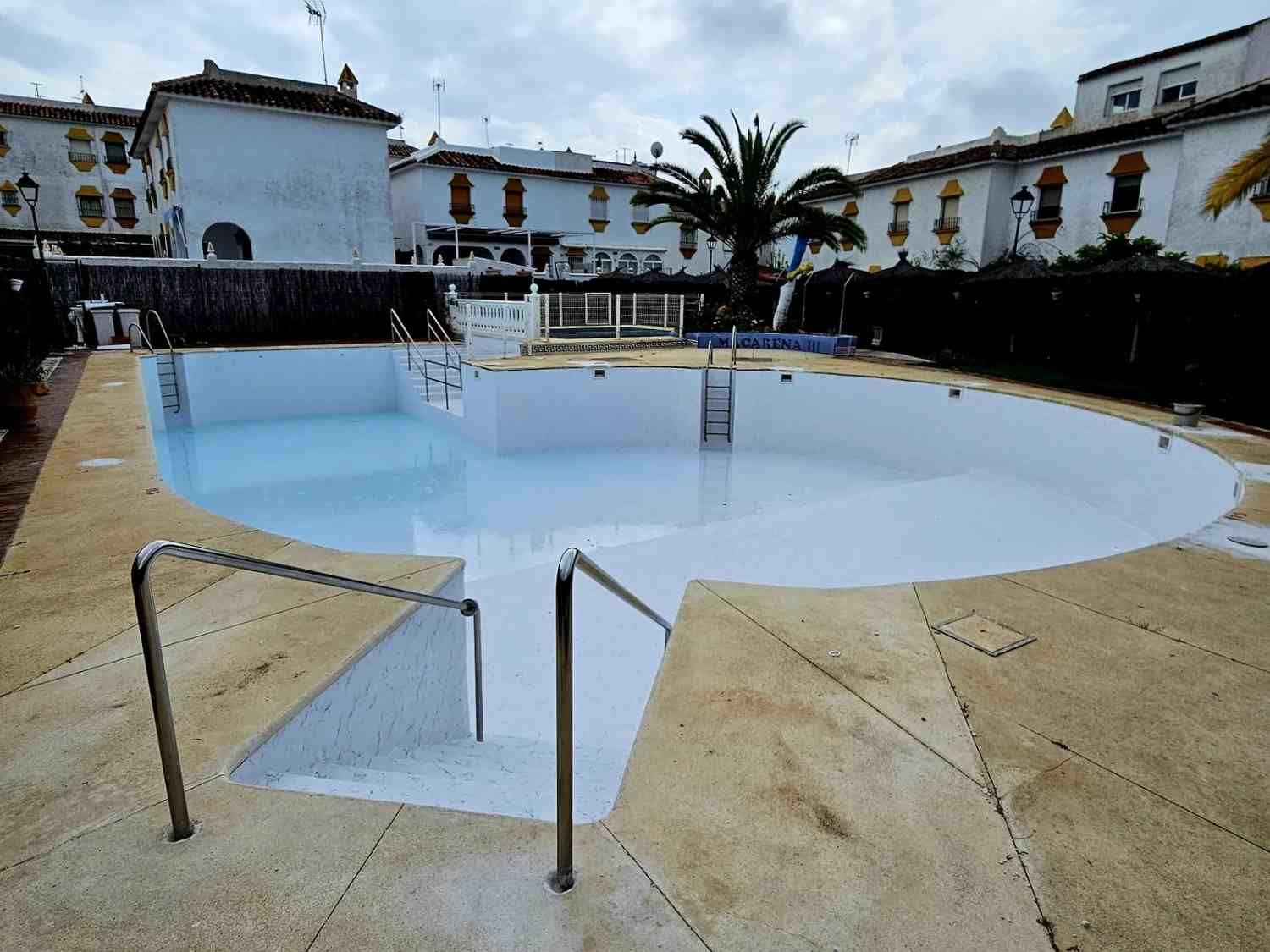 Piscina exterior vacía, con un vaso blanco curvo y edificios blancos alrededor.