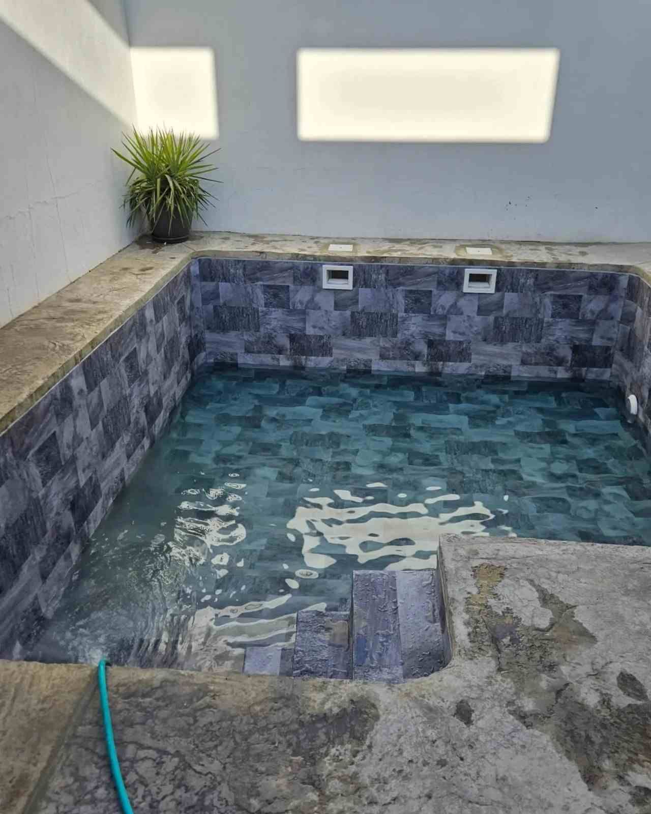 Pequeña piscina de inmersión cubierta, revestida de azulejos, con agua azul y borde de piedra, vista desde arriba