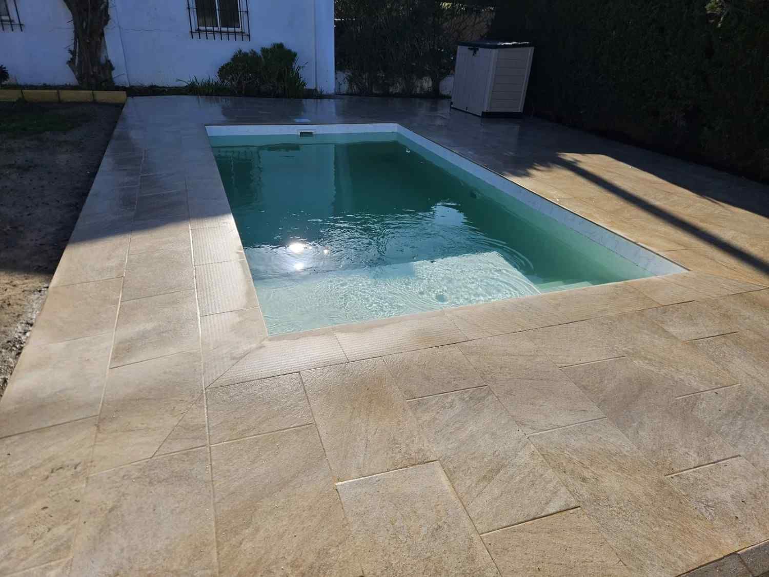Piscina rectangular al aire libre con una terraza de piedra clara en un patio trasero soleado