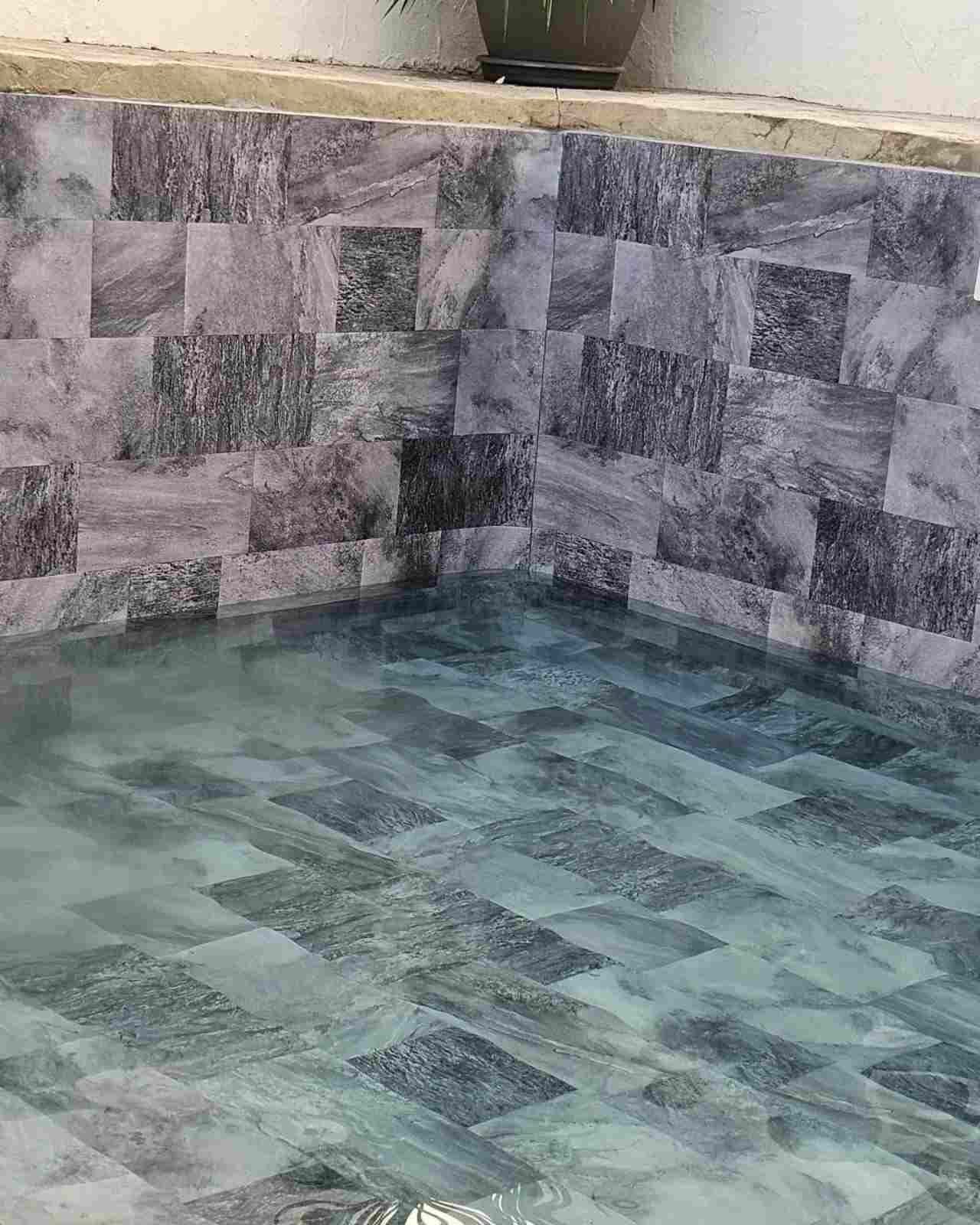 Esquina de piscina o fuente con azulejos de piedra, agua azul verdosa y paredes grises con motivos decorativos