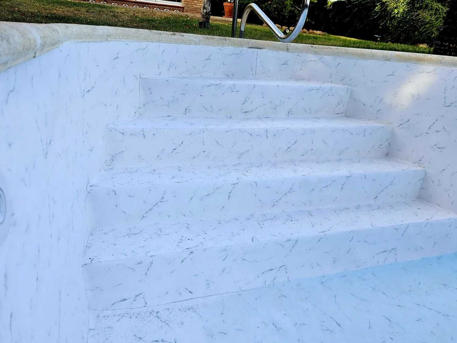 Escalones de hormigón blanco que conducen a una piscina vacía y sin agua, con una barandilla metálica.