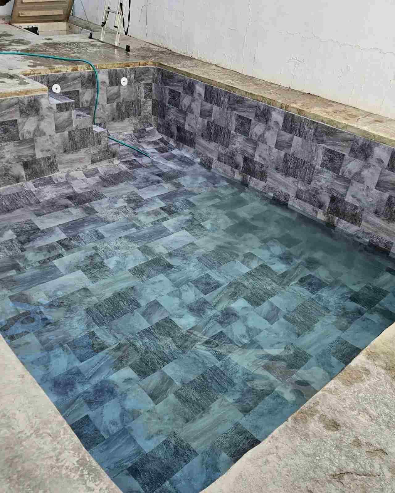Piscina o spa de azulejos vacía, con interior de mosaico azul grisáceo y borde de piedra