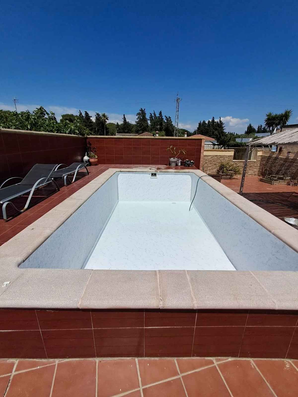 Piscina enterrada vacía, con el interior blanco y el borde de baldosas rojas, bajo un cielo azul despejado