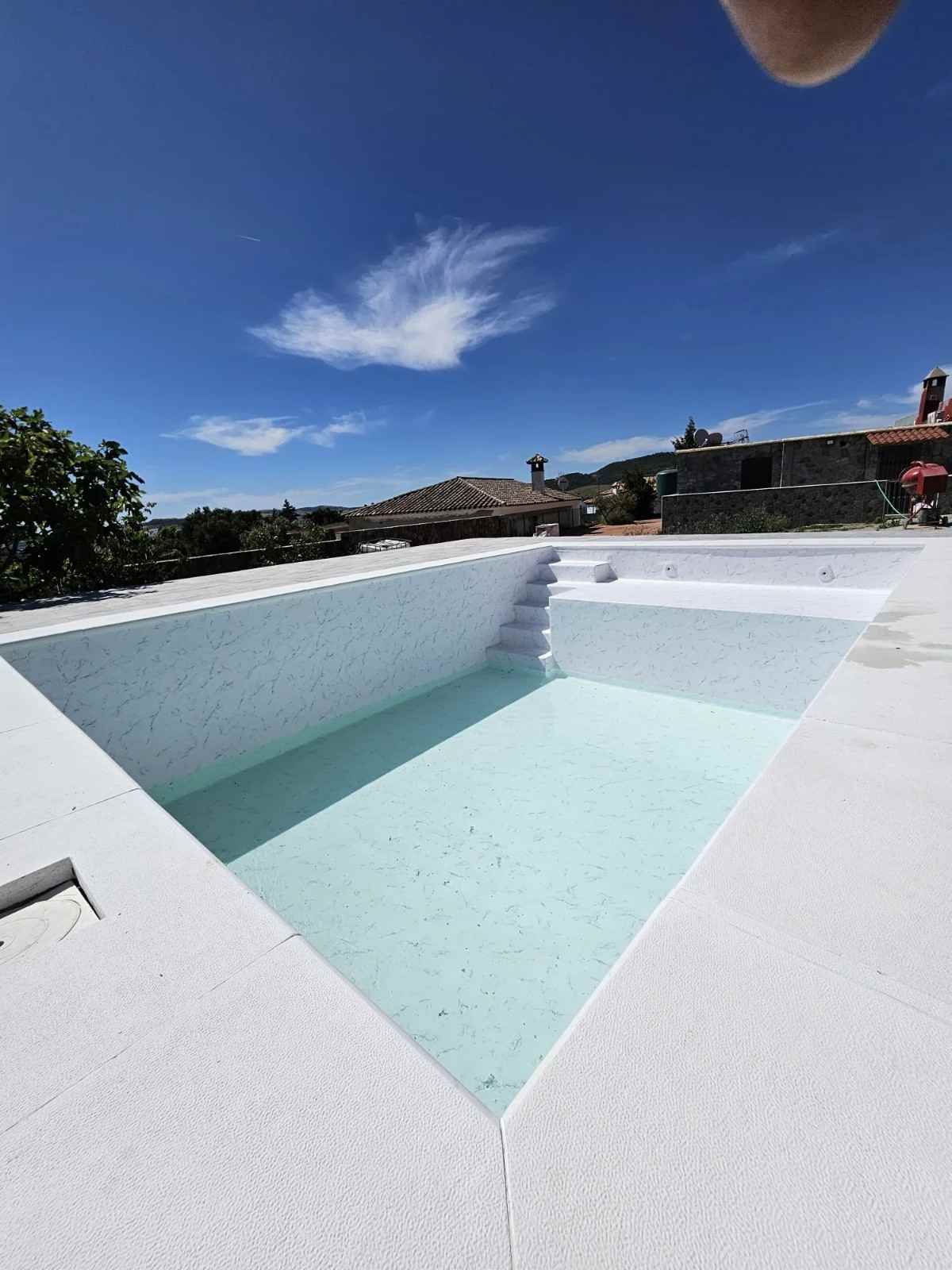 Piscina blanca de formas geométricas, con agua azul claro bajo un cielo azul despejado