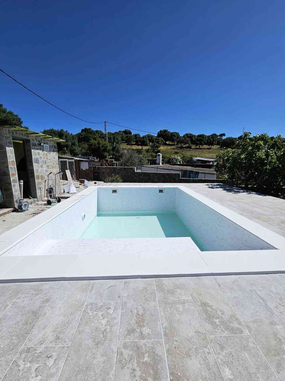 Piscina vacía y blanca con agua azul claro, al aire libre bajo un cielo azul despejado.