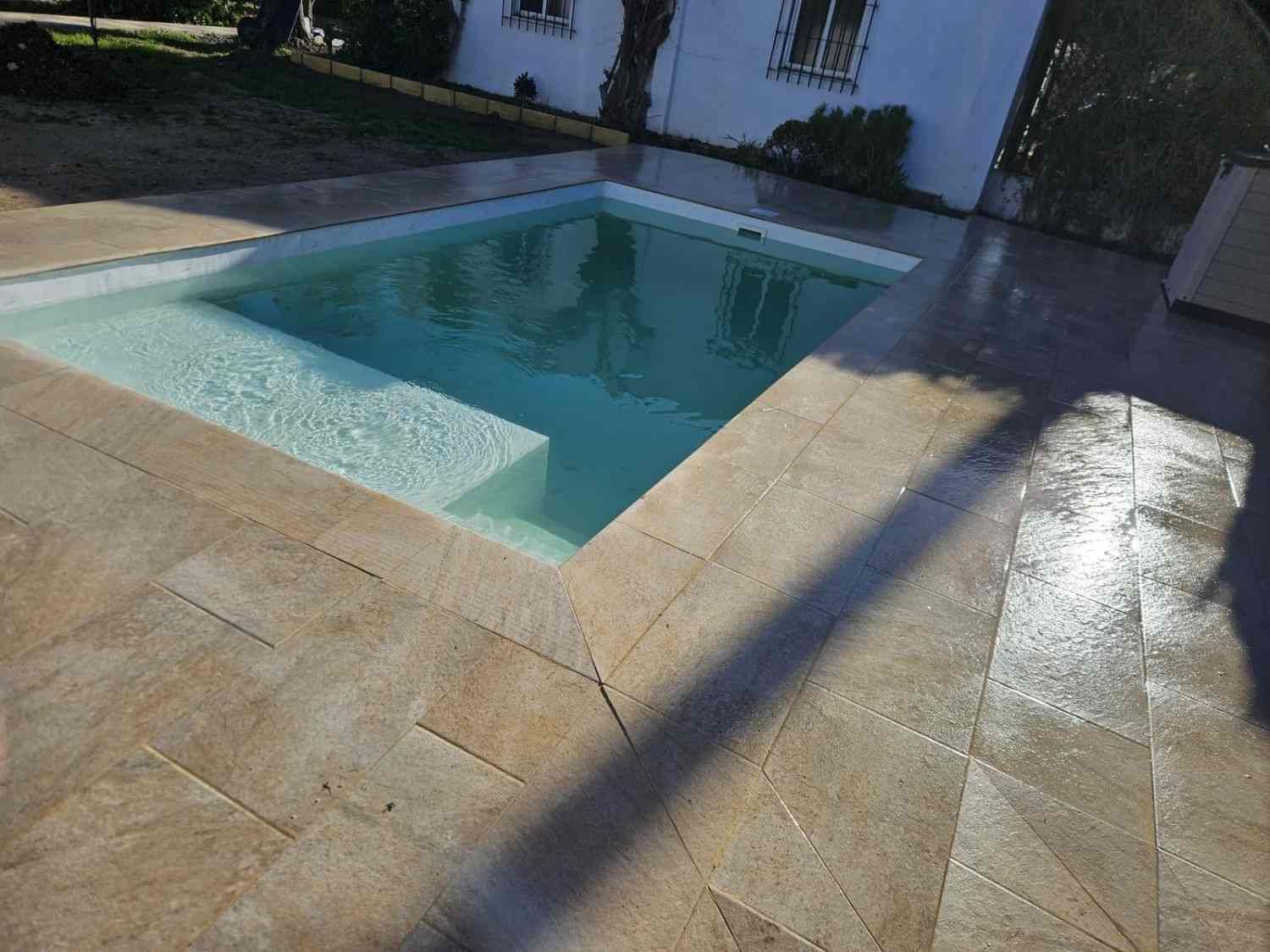 Patio trasero con una pequeña piscina rectangular y la luz del sol proyectando sombras alargadas.