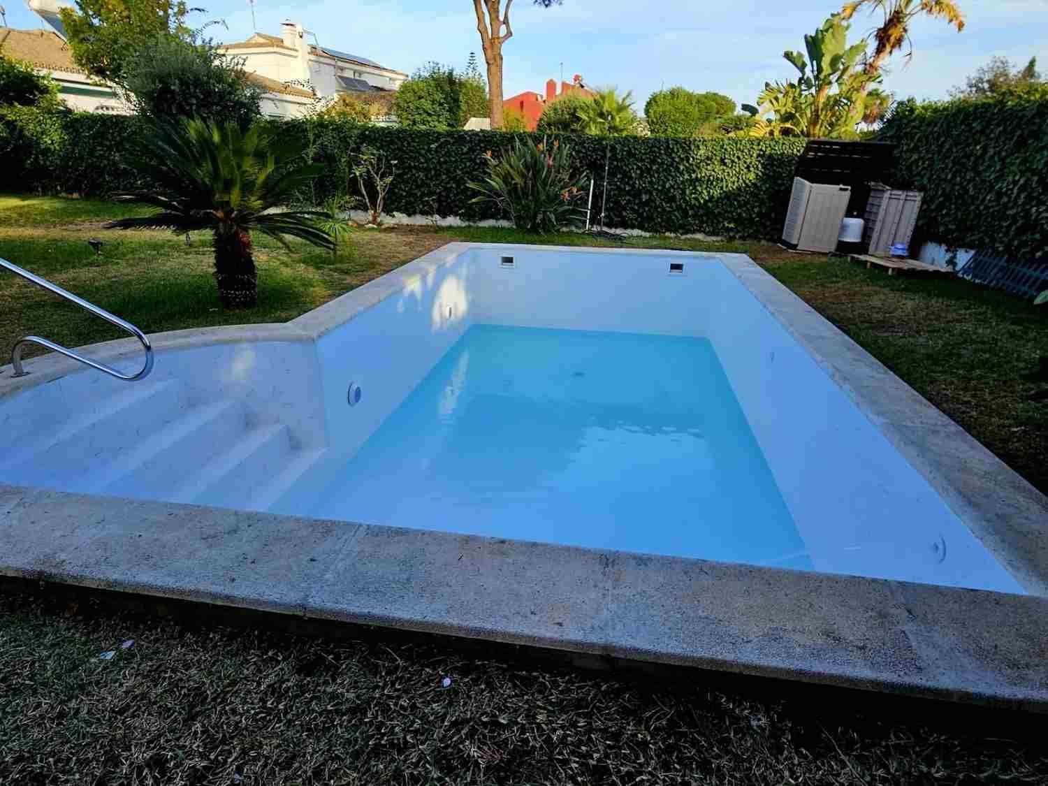Piscina rectangular vacía en el jardín trasero, con agua azul y escalones blancos, rodeada de césped y árboles