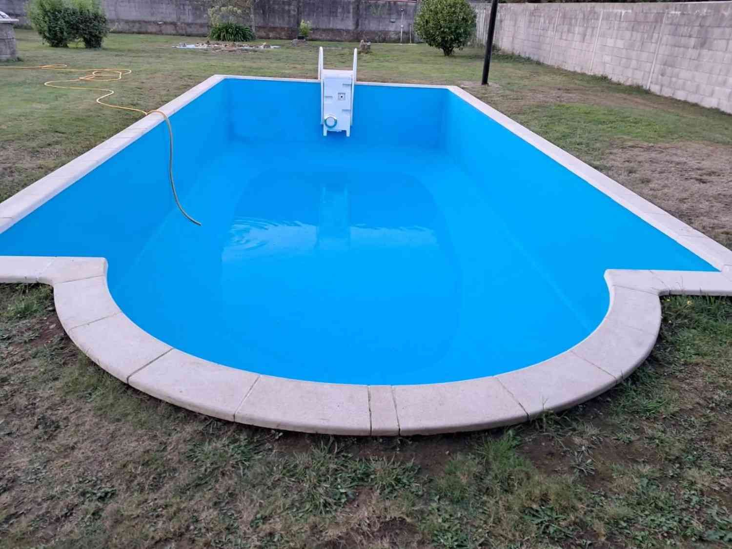 Piscina vacía de color azul con un tobogán en un patio trasero, vista desde la zona menos profunda.