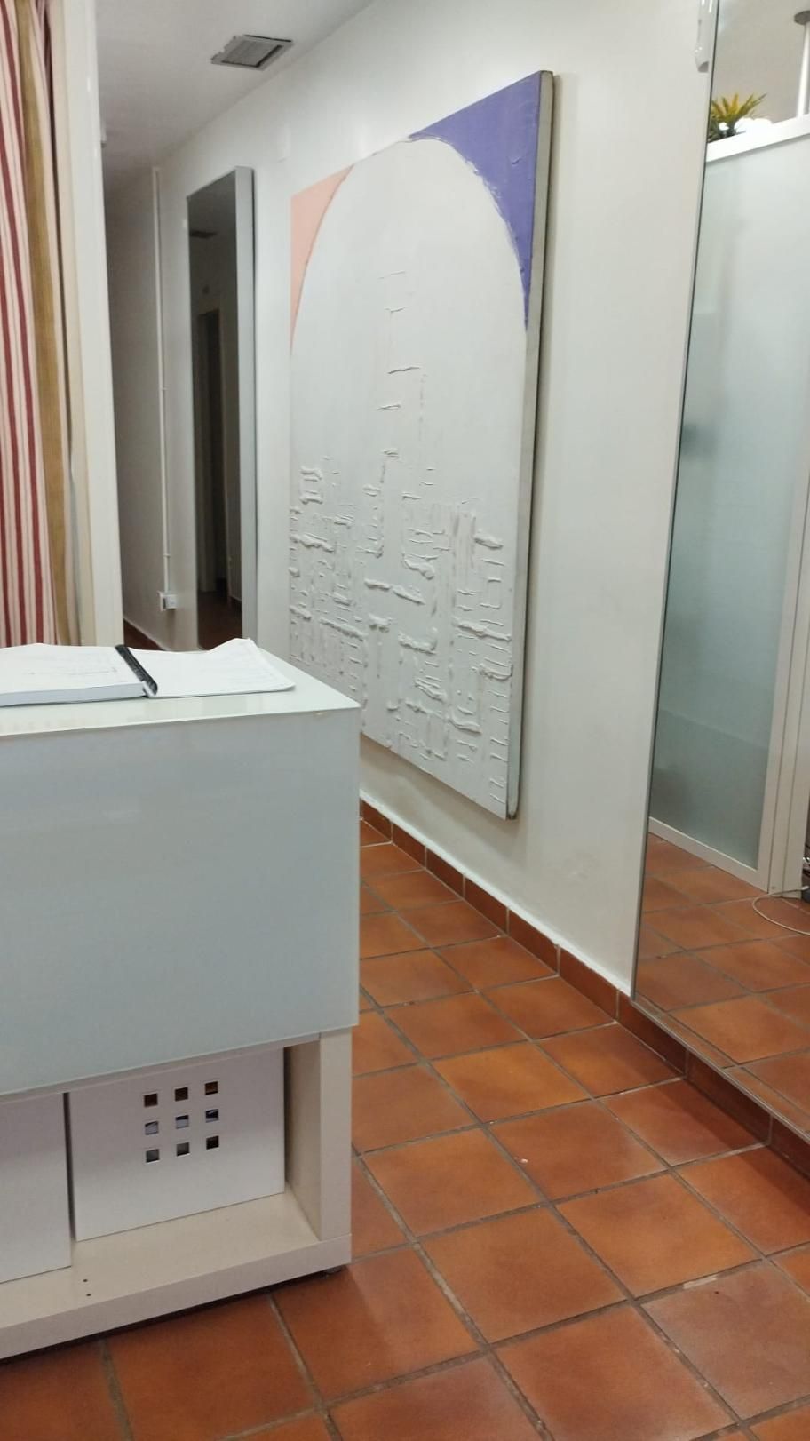 Área de recepción con escritorio blanco, arte abstracto, piso de baldosas y espejo.