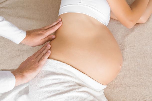 Des mains massent un ventre de femme enceinte sur une surface recouverte d'une serviette blanche