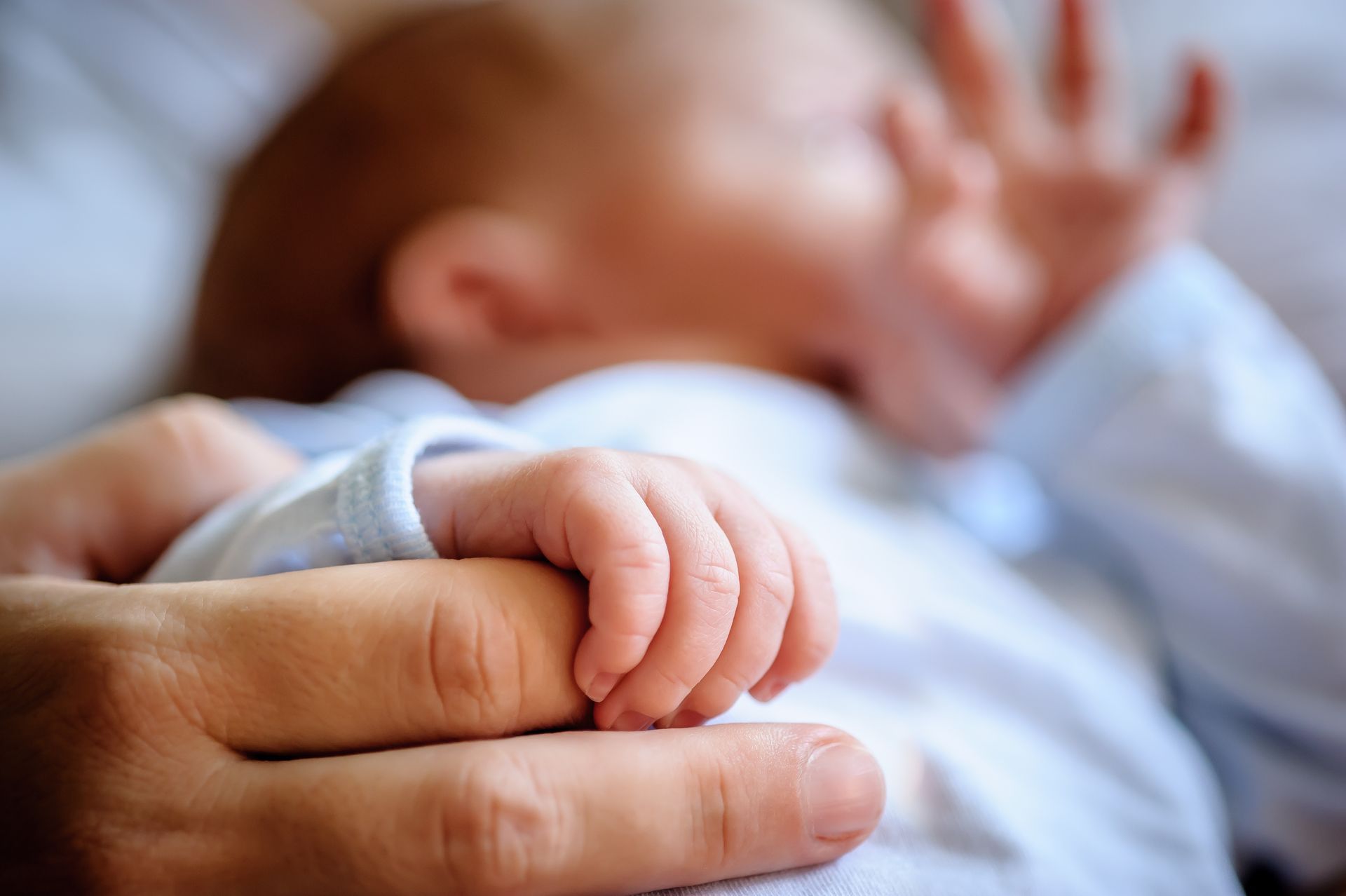 Une main d'adulte tenant la petite main d'un bébé, ce dernier étant doucement flouté en arrière-plan.