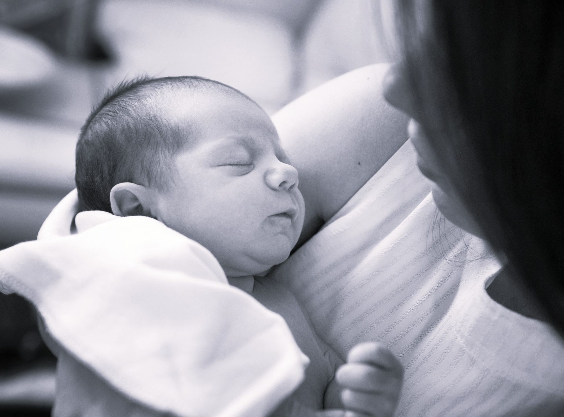 Un bébé endormi dans les bras d'un adulte, dans des tons doux de noir et blanc.