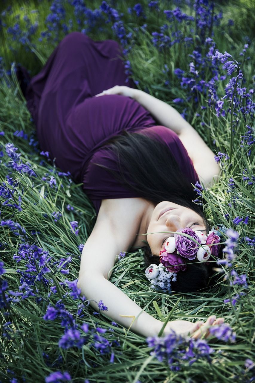 Femme en robe violette allongée dans un champ de fleurs violettes, portant une couronne de fleurs.