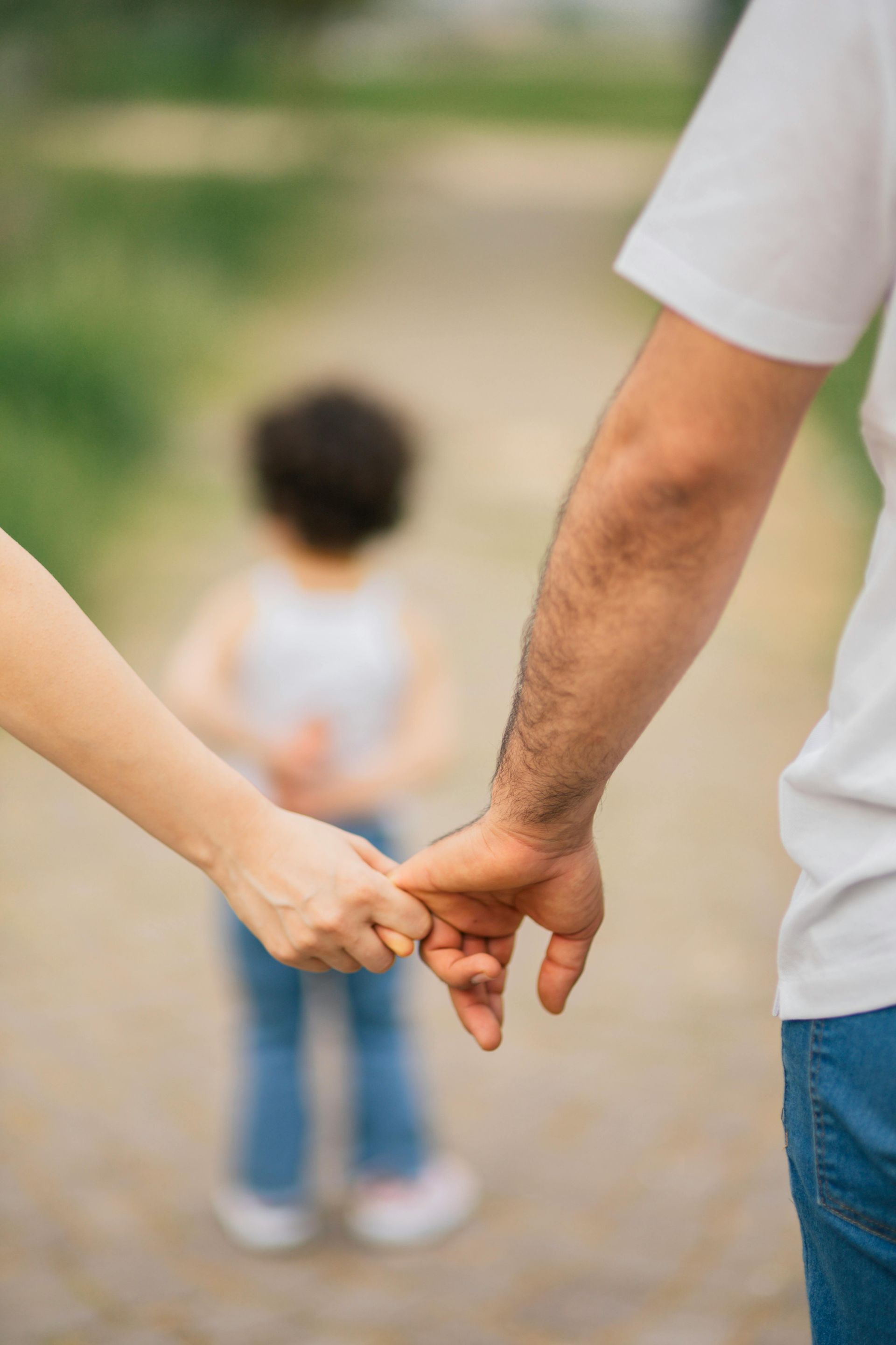 Des adultes tenant la main d'un enfant tout en marchant sur un chemin extérieur flou