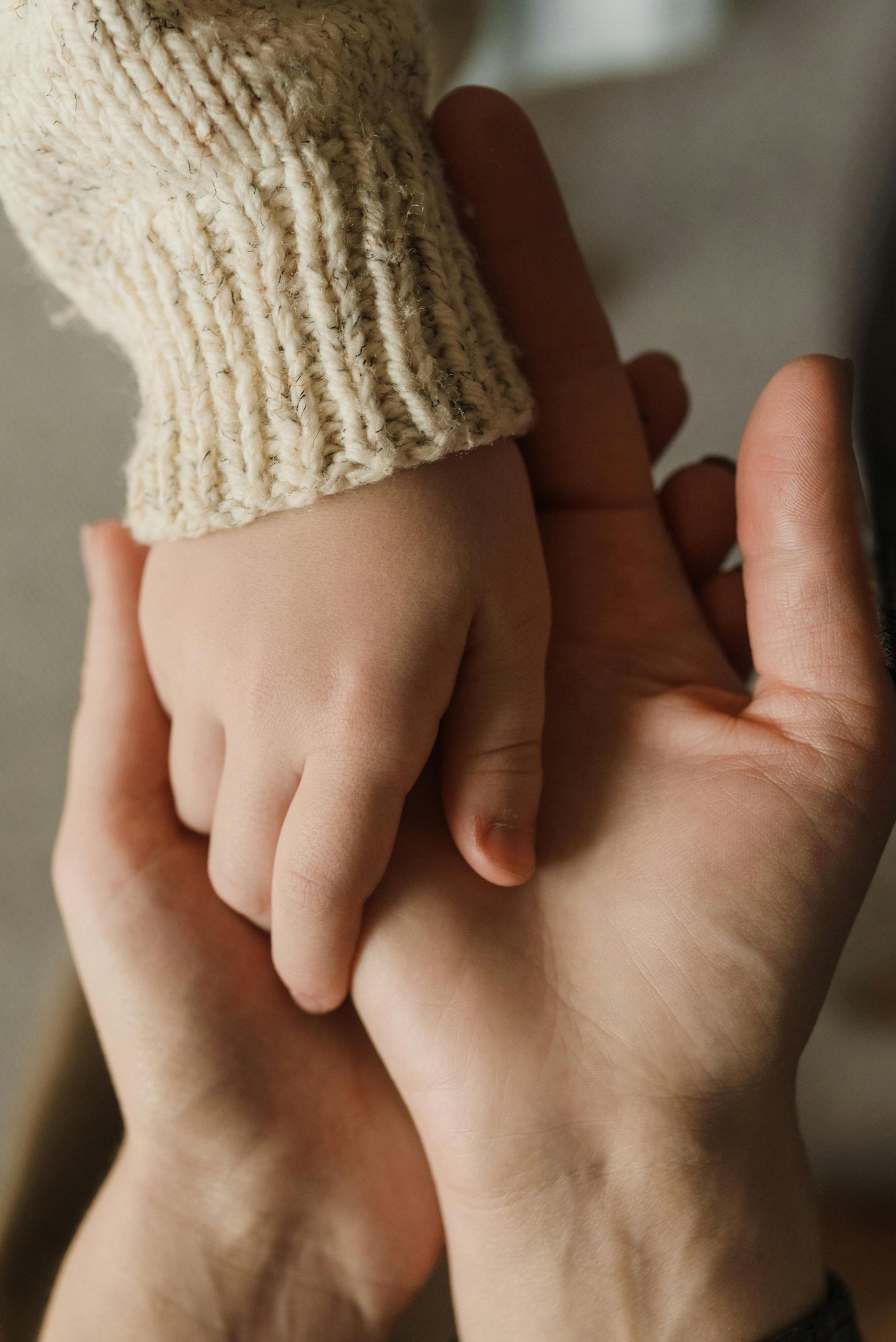 Des mains d'adulte et d'enfant se tenant doucement dans une douce lumière naturelle