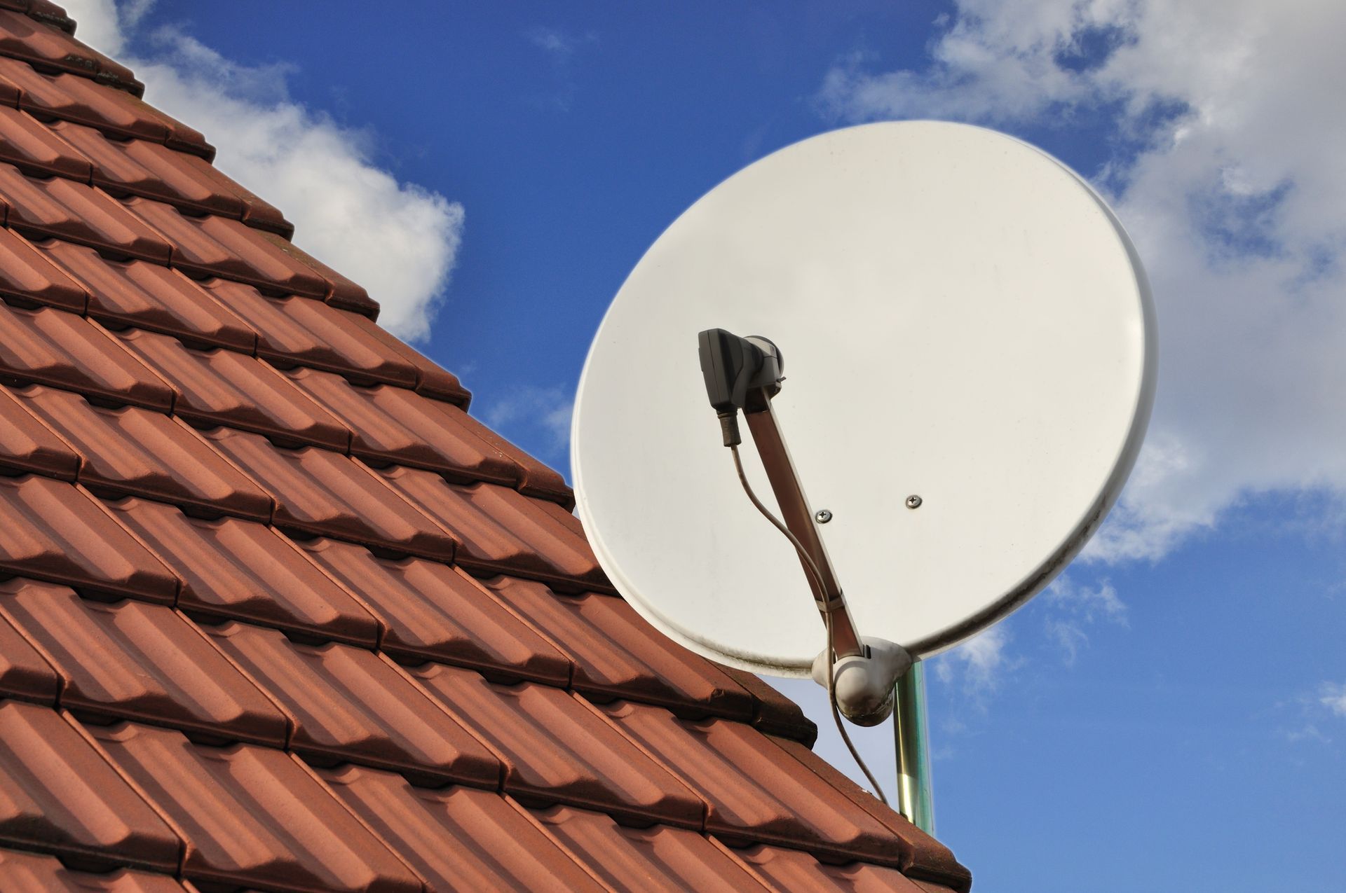 Antenne parabolique blanche sur un toit de tuiles rouges, se détachant sur un ciel bleu.