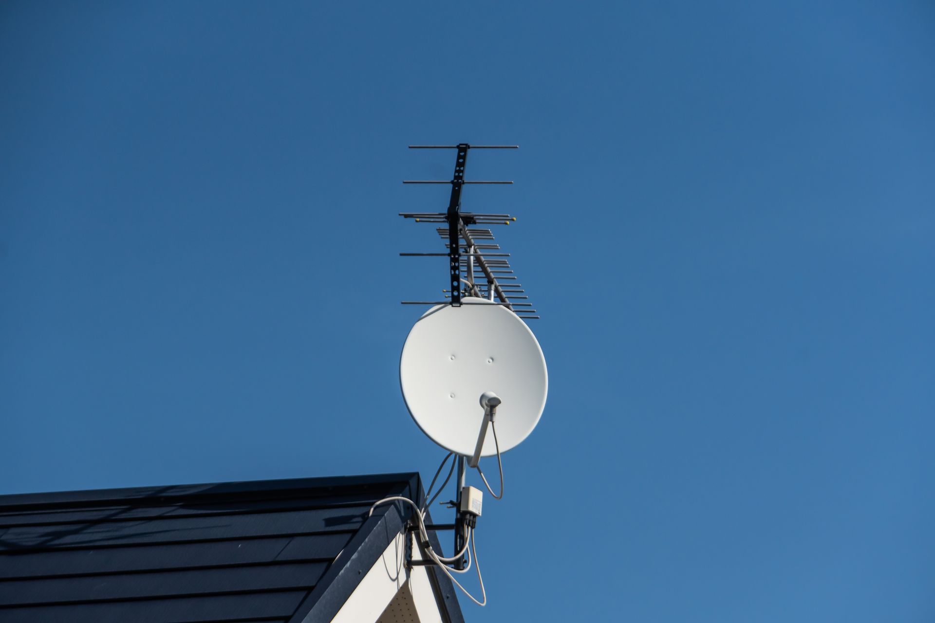 Antenne parabolique et antenne TV installées sur un toit, se détachant sur un ciel bleu dégagé.