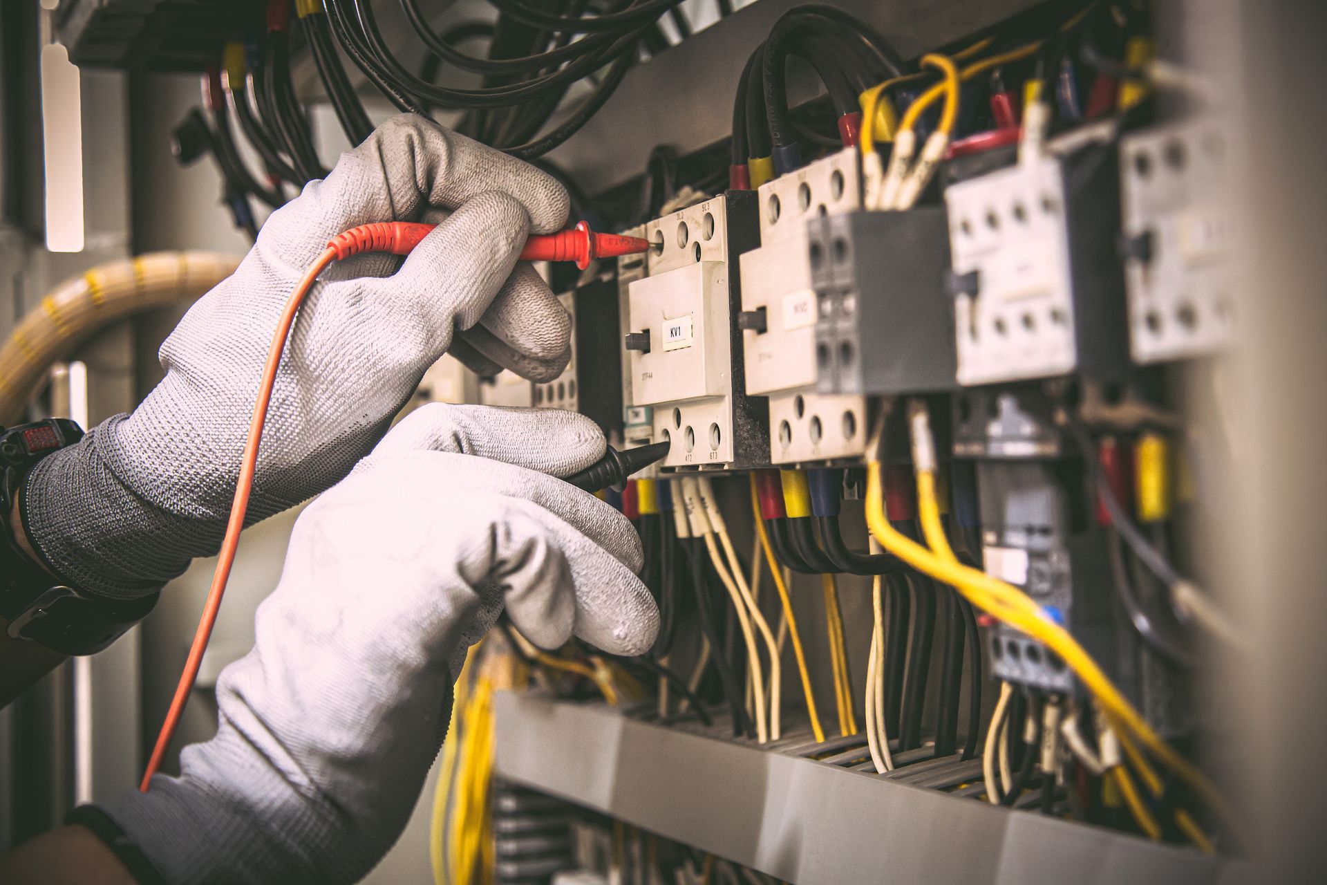 Des mains gantées testent les fils d'un panneau de commande électrique comportant des interrupteurs et des câbles.