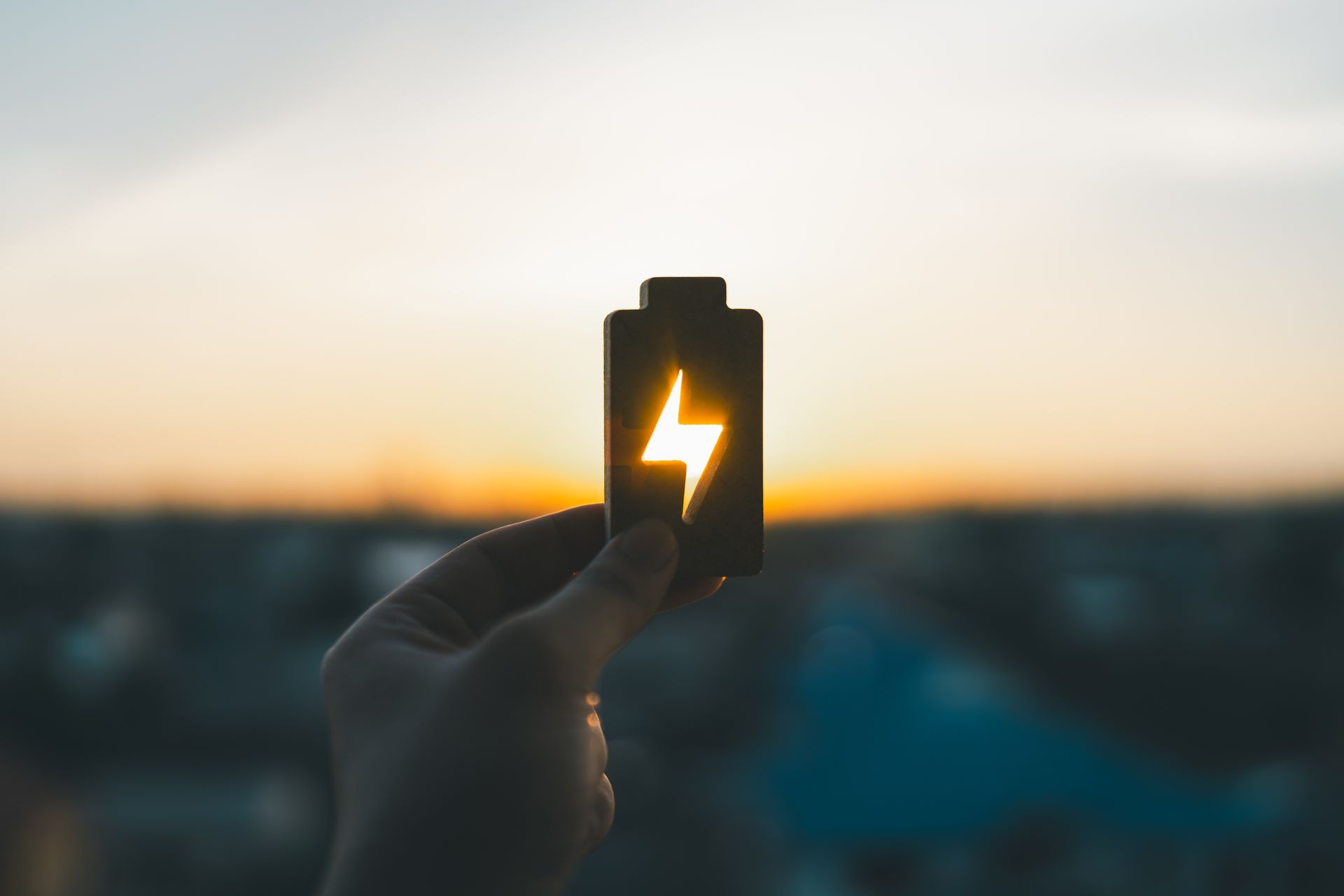Main tenant une icône de batterie avec un symbole d'éclair lumineux sur un ciel de coucher de soleil flou