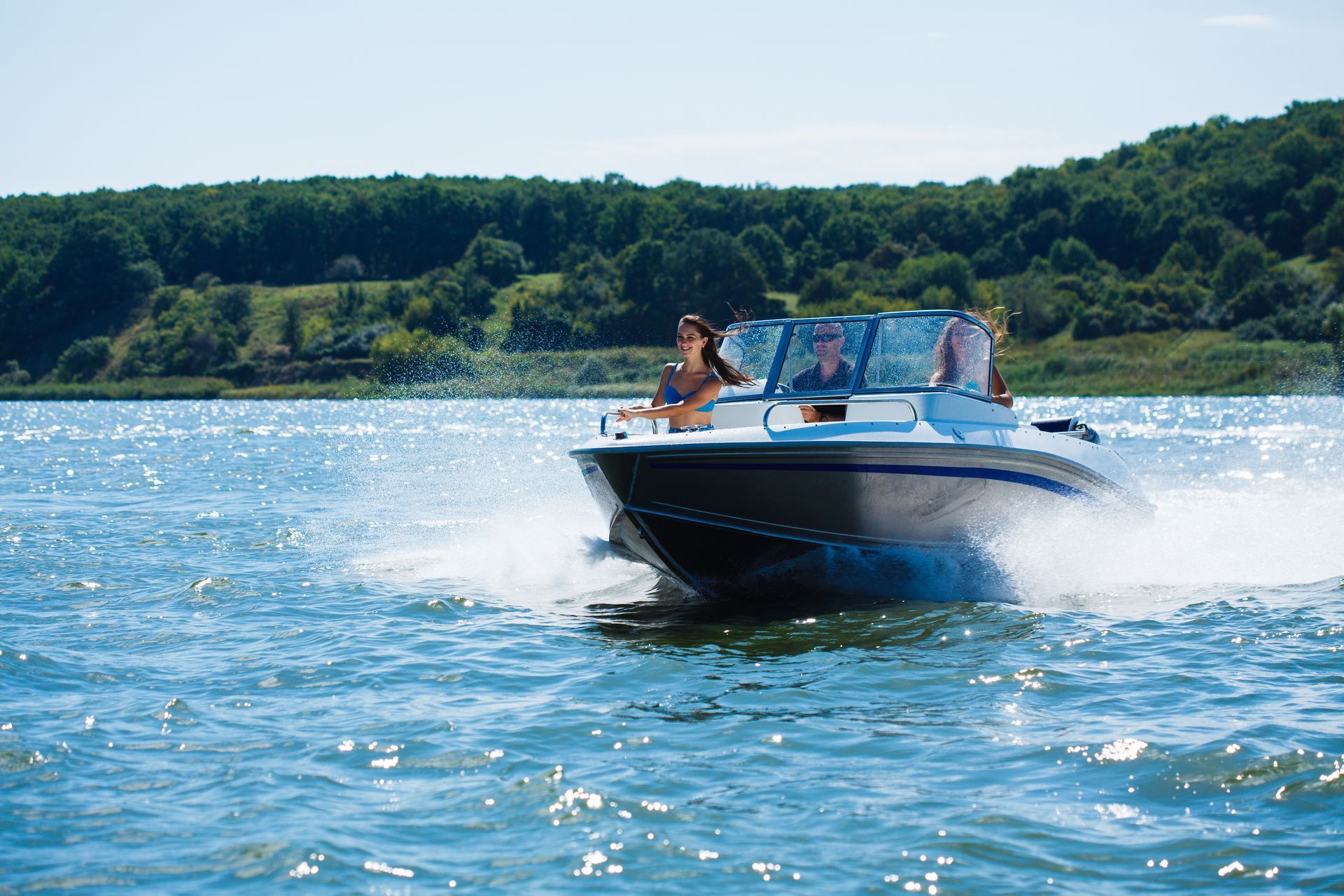Un hors-bord file à toute allure sur l'eau bleue avec deux personnes à bord et une côte verdoyante en arrière-plan.