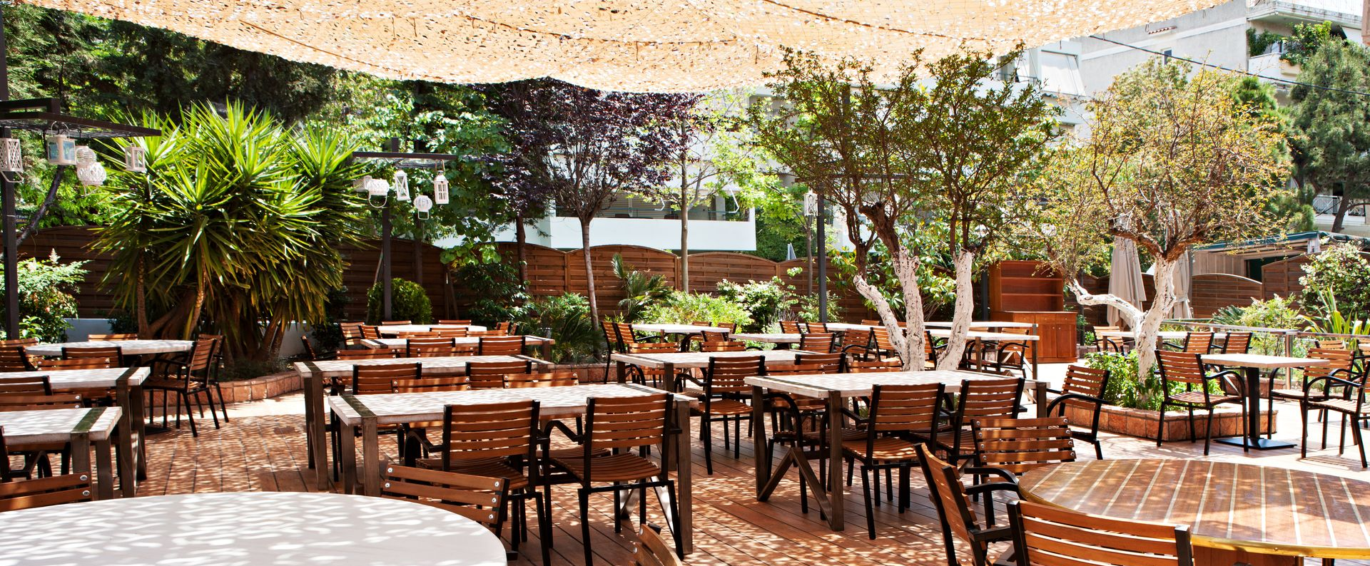 Terrasse de café avec tables et chaises en bois sous les arbres et les voiles d'ombrage