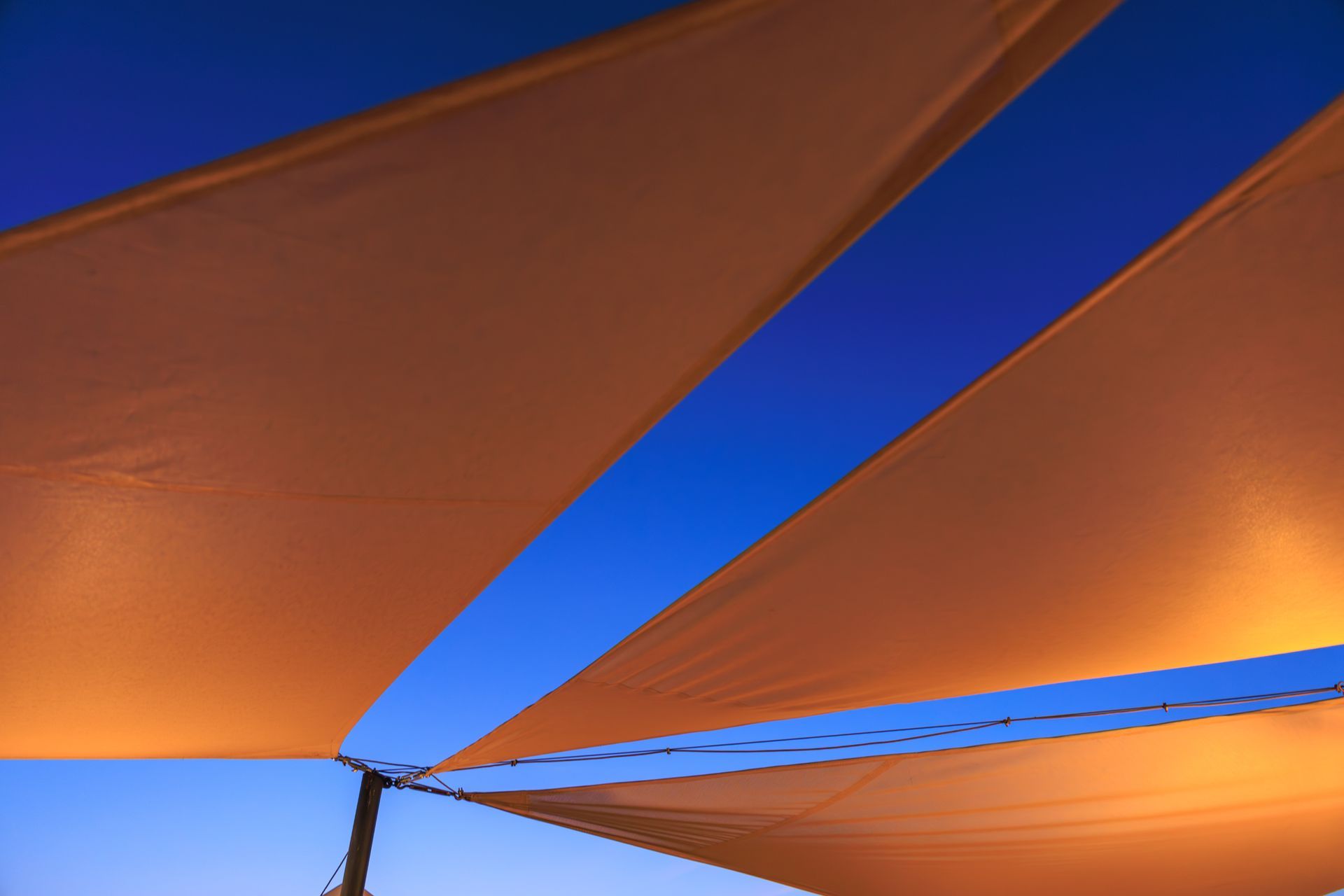 Des voiles triangulaires orange se détachent sur un ciel bleu au coucher du soleil.