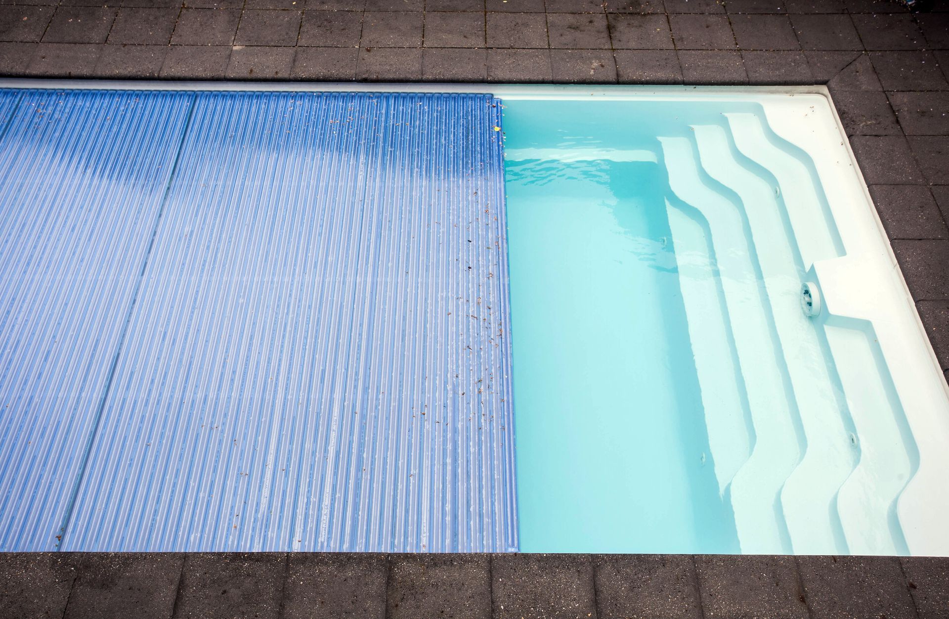 Une bâche bleue recouvre partiellement une piscine avec des marches.