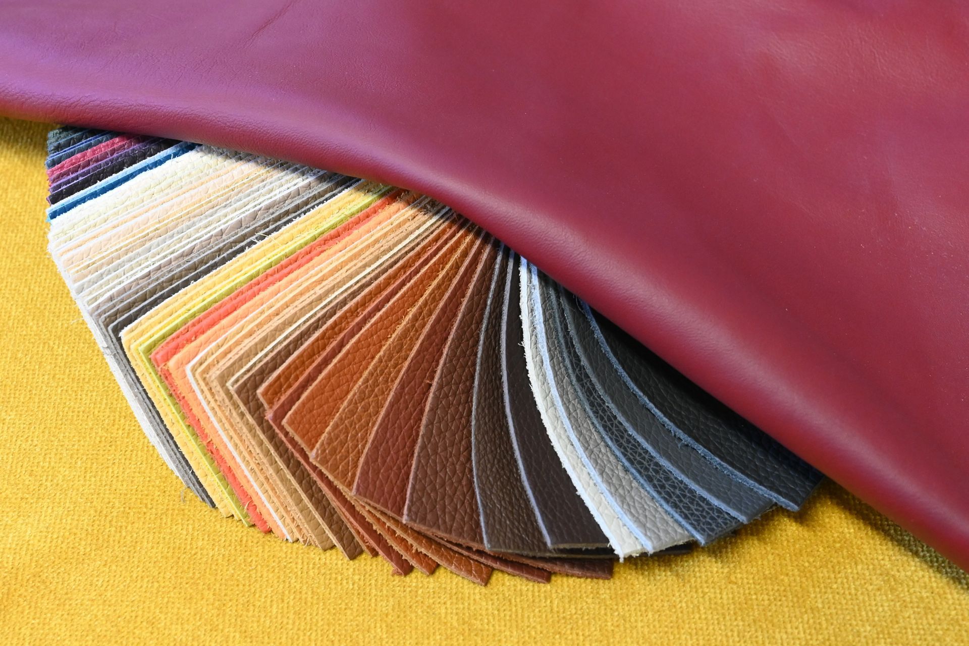 Éventail d'échantillons de cuir colorés sur une surface jaune sous une pièce de cuir bordeaux.