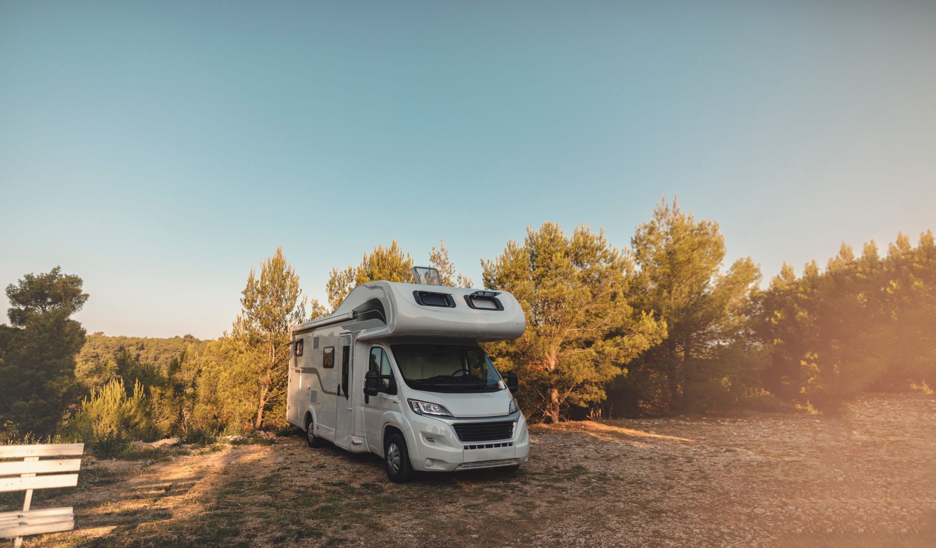 Un camping-car blanc garé dans un emplacement de camping, à l'ombre des arbres. 