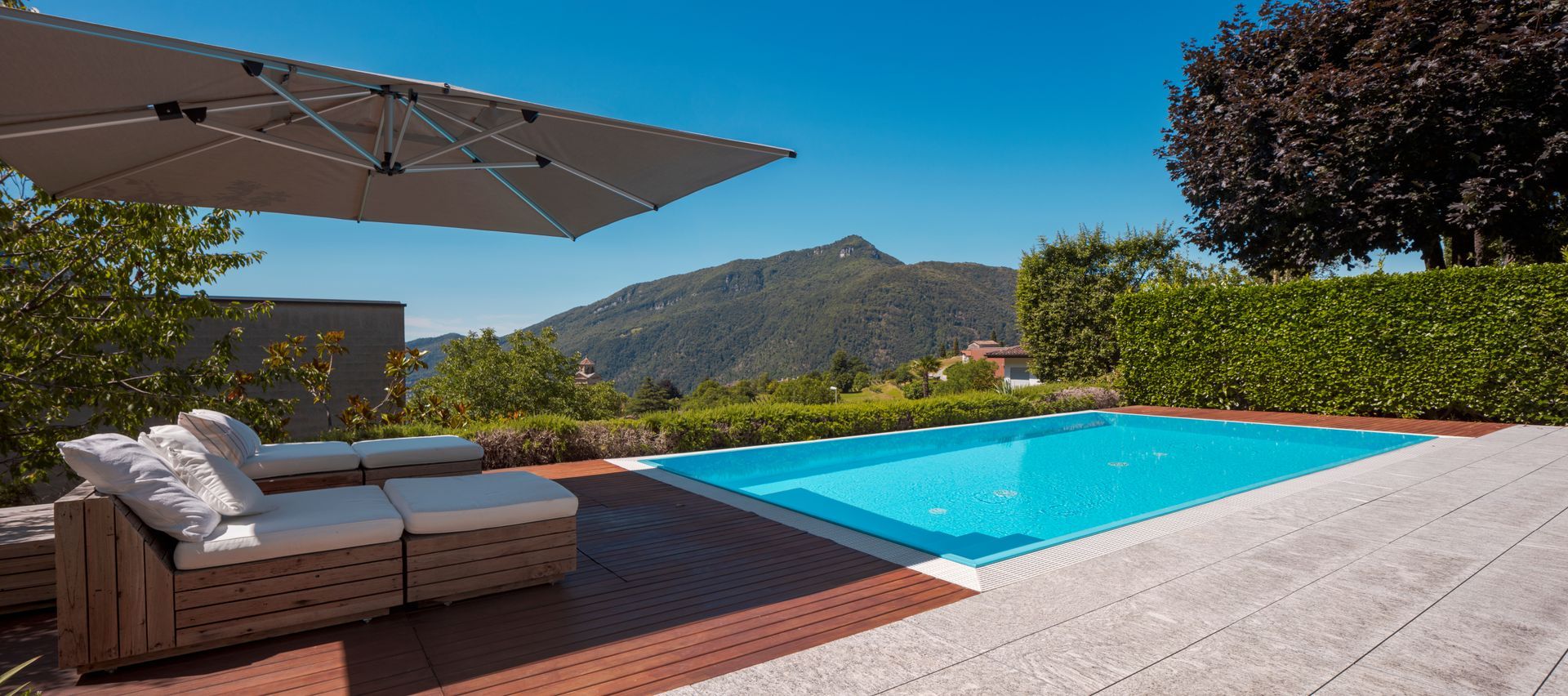 Terrasse moderne dans le jardin avec parasol, chaises longues et piscine donnant sur les montagnes