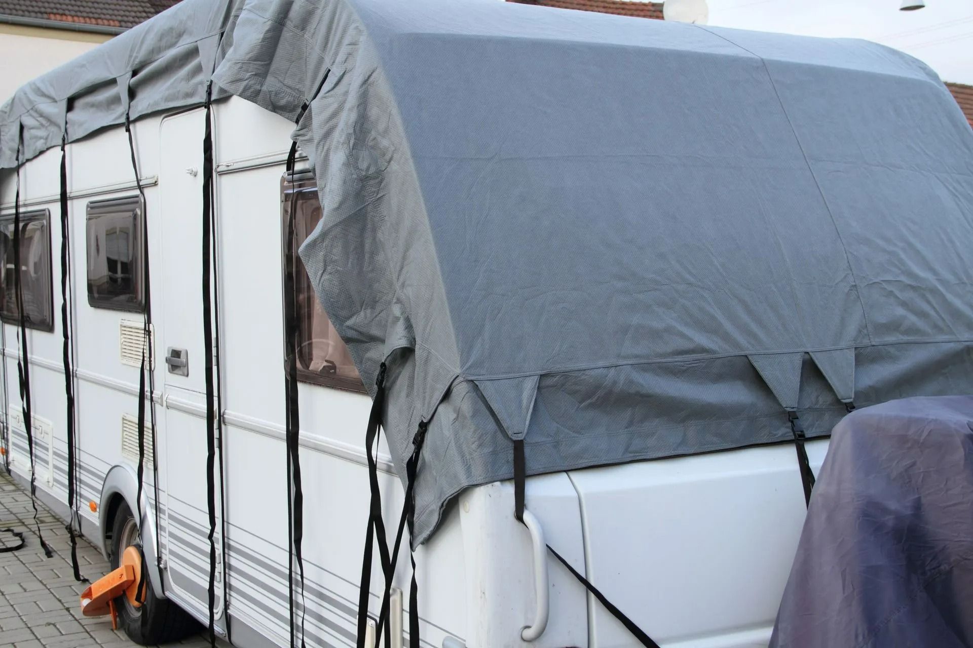 Caravane blanche recouverte d'une bâche grise, garée à l'extérieur.