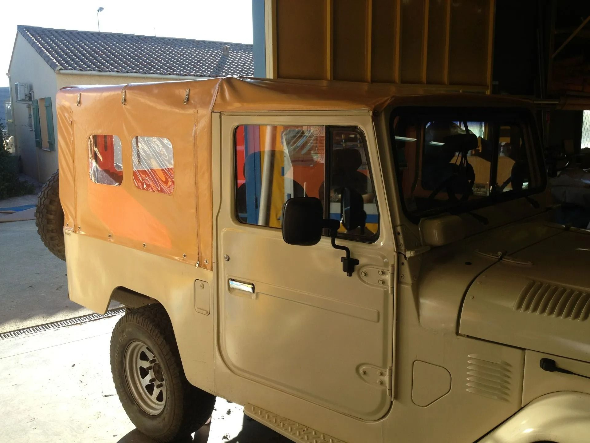Un camion vintage beige avec une bâche orange est stationné dans un garage.