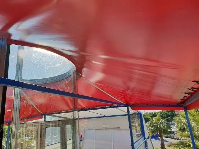 Bâche rouge posée sur une structure métallique bleue à côté d'un bâtiment en verre et de palmiers