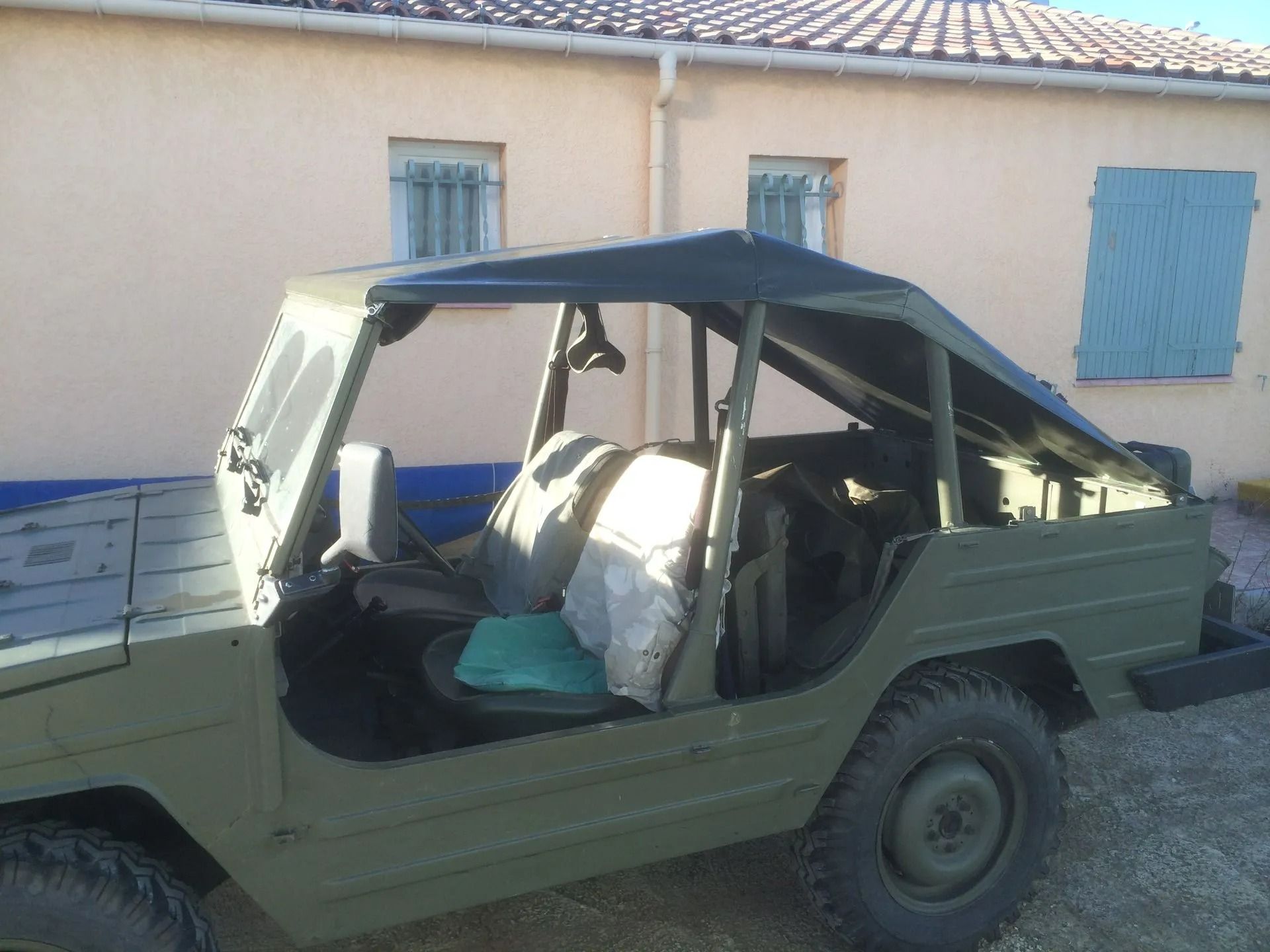 Petite voiture décapotable stationnée à côté d'une habitation aux volets bleus.
