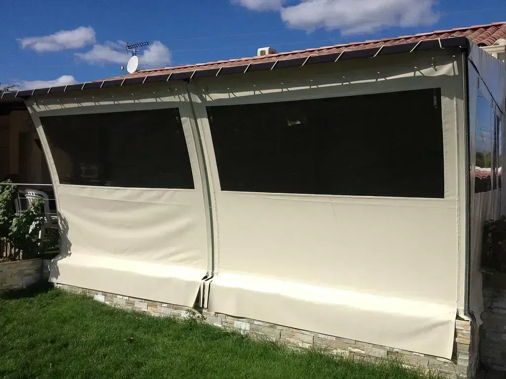 Auvent de terrasse blanc avec panneaux latéraux en vinyle transparent, fixé à une maison donnant sur une cour gazonnée.