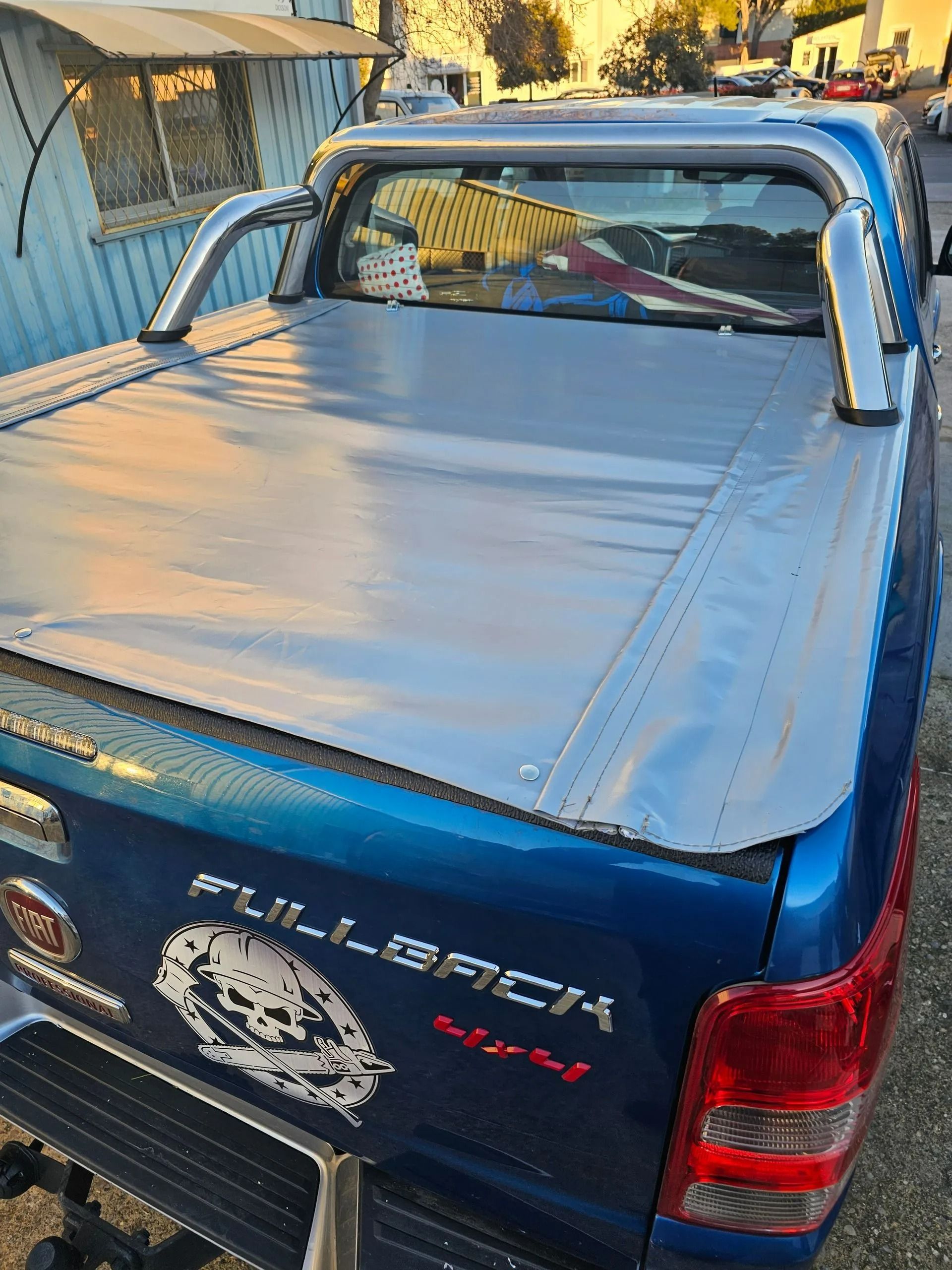 Pick-up avec une bâche argentée garée près d'un bâtiment.