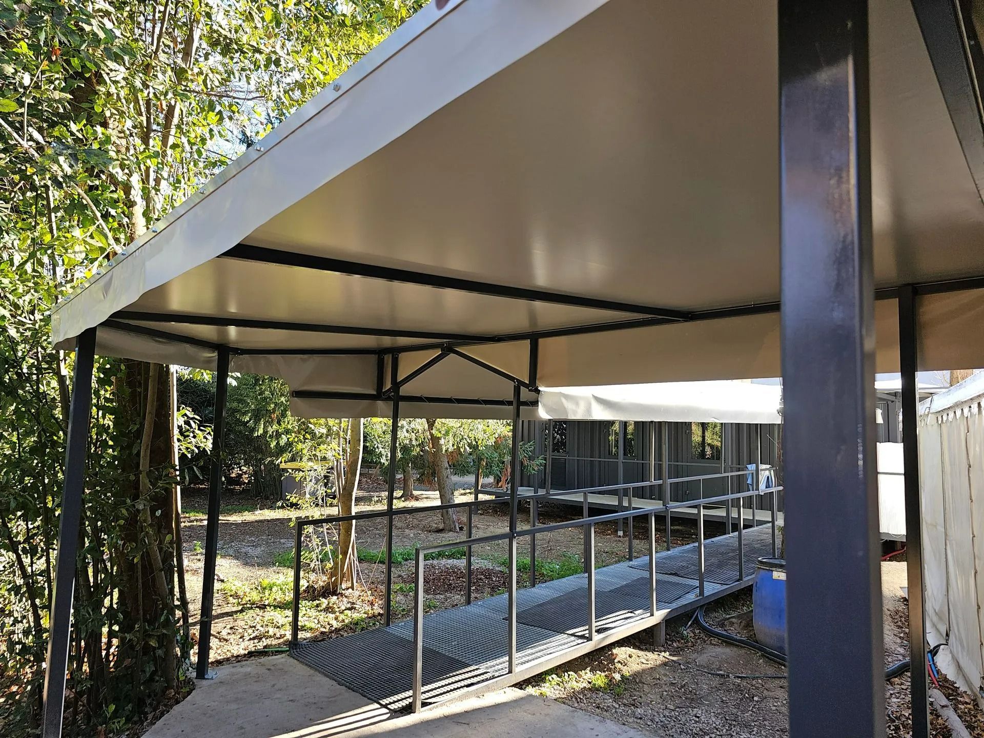Rampe d'accès couverte avec garde-corps métalliques, à côté d'un bâtiment et d'arbres à l'extérieur