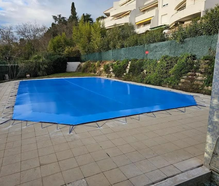 Piscine extérieure couverte jouxtant une terrasse et une haie dans un quartier résidentiel