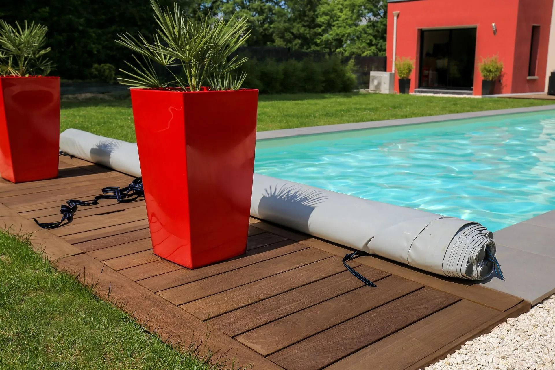 Terrasse au bord de la piscine avec jardinières rouges et bâche de piscine enroulée près de l'eau
