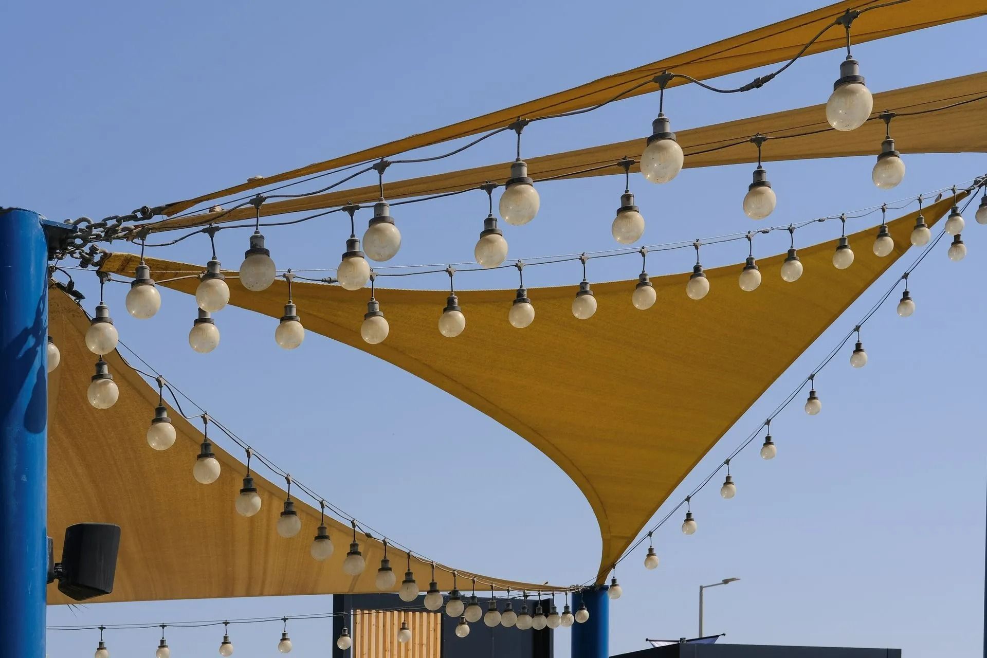Voiles d'ombrage jaunes ornées de guirlandes lumineuses se détachant sur un ciel bleu clair.