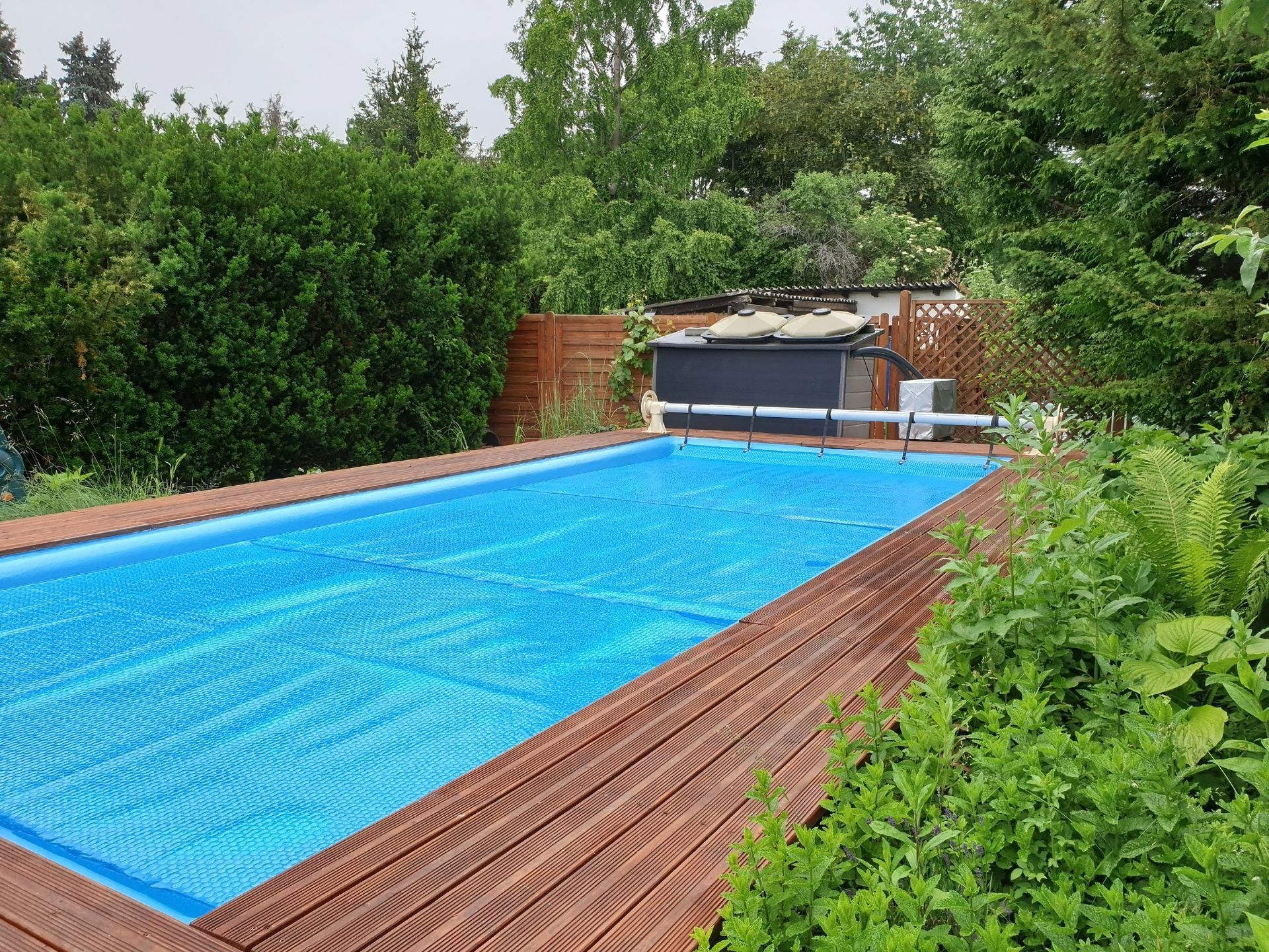 Piscine extérieure couverte, entourée d'une terrasse en bois et d'une végétation luxuriante.