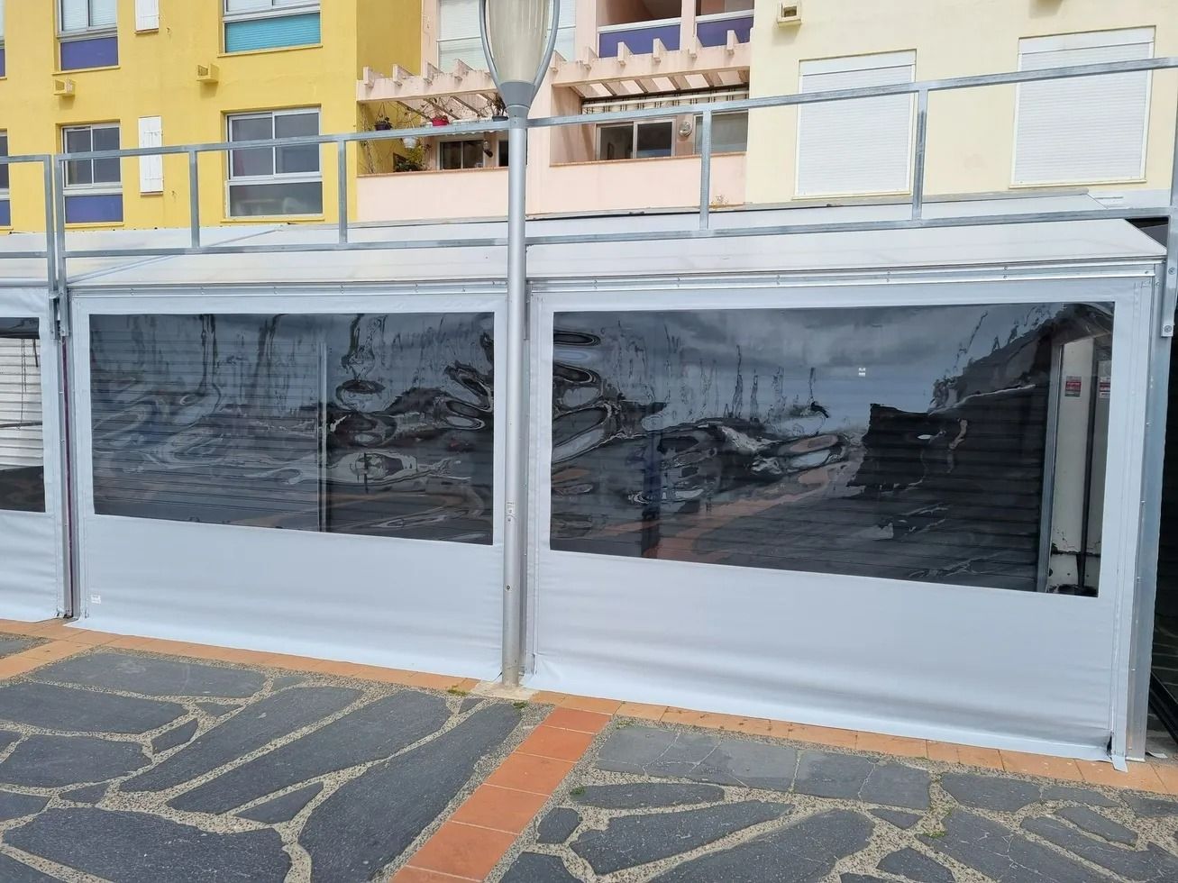 Terrasse donnant sur un trottoir, fermée par des bâches transparentes et blanches 