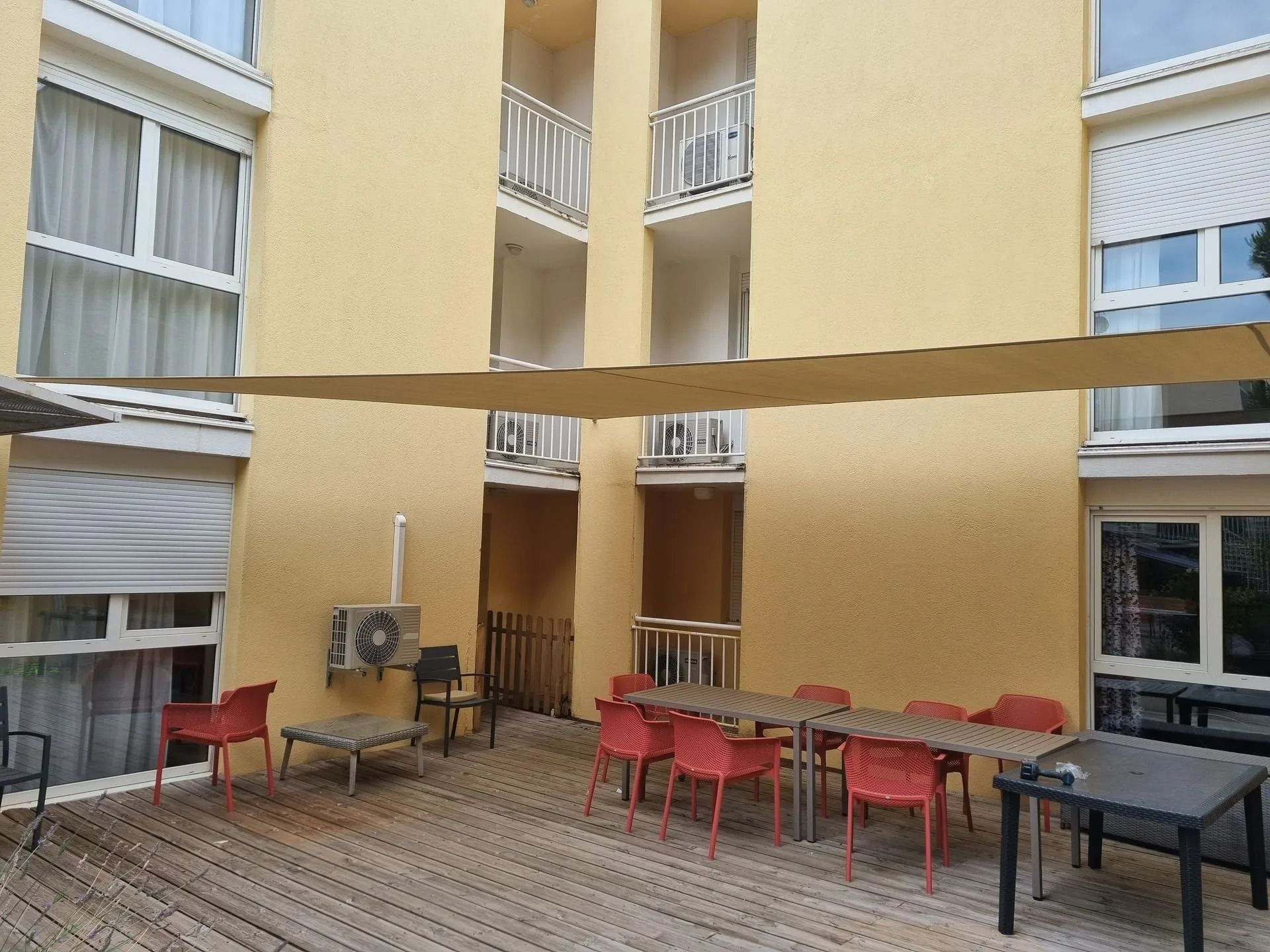 Terrasse extérieure avec tables et chaises orange couvertes par une bâche beige entre les immeubles 