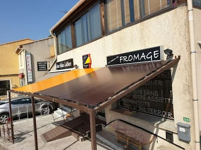Façades de boutiques avec auvent noir et orange et enseignes noires, dont une FROMAGE