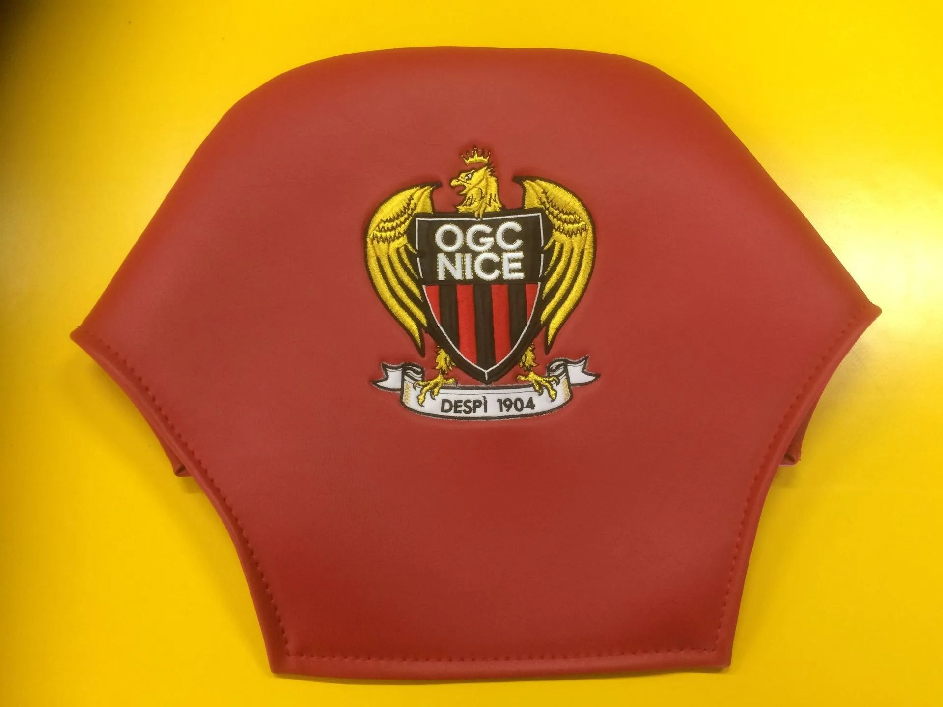 Écusson OGC Nice incrusté sur une surface rouge et posé sur un fond jaune