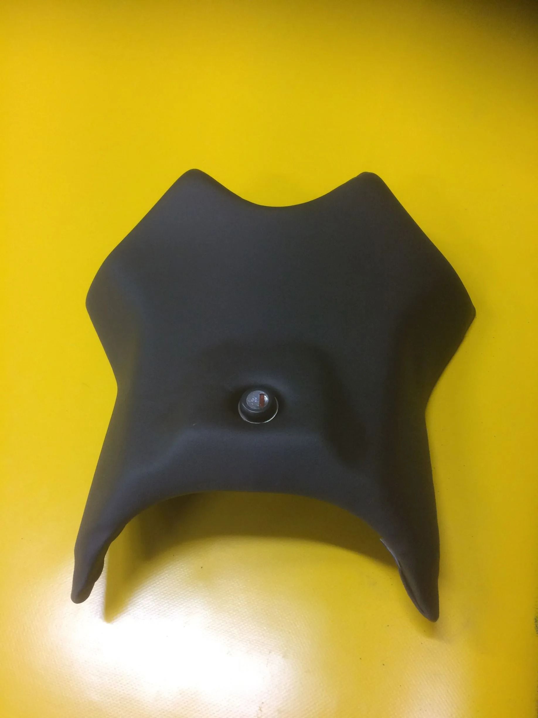 Objet en plastique noir incurvé avec un bouton central sur fond jaune