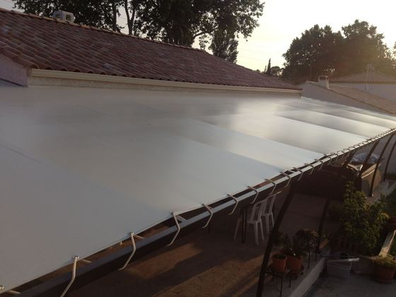 Une bâche blanche est tendue  au-dessus d'un patio, à côté d'un toit de tuiles