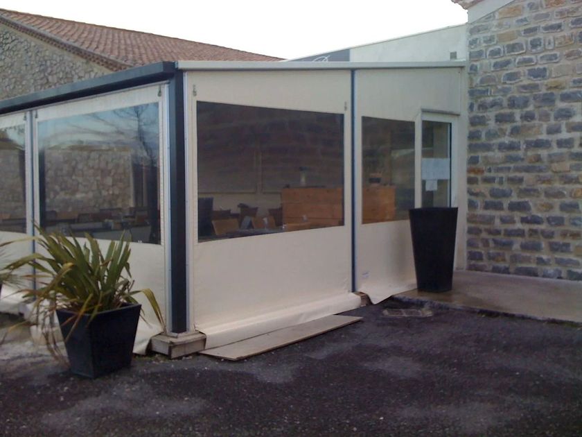 Terrasse adossée à un mur en pierre fermée par des bâches 