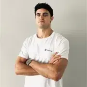 Un hombre con una camiseta blanca está de pie con los brazos cruzados.